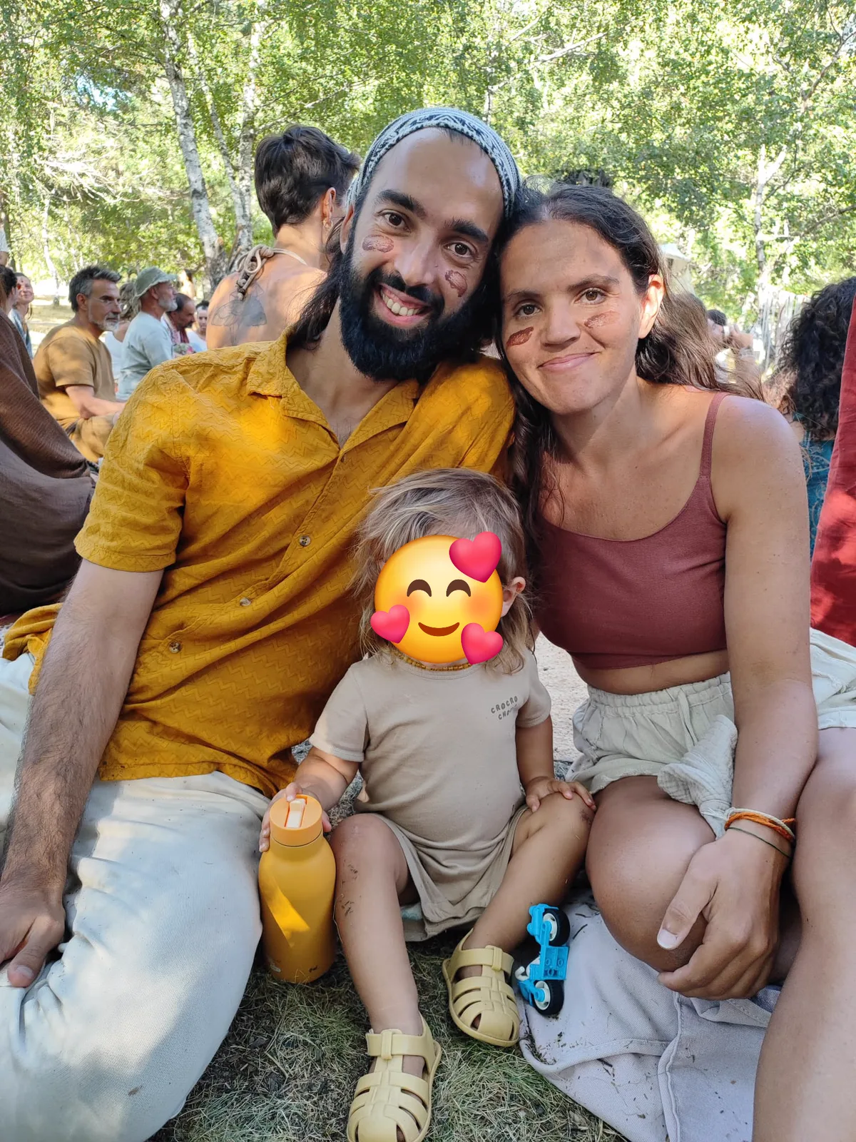 Tiago, Irina and their son sitting together on the grass at a gathering, cacao marks on their cheeks.