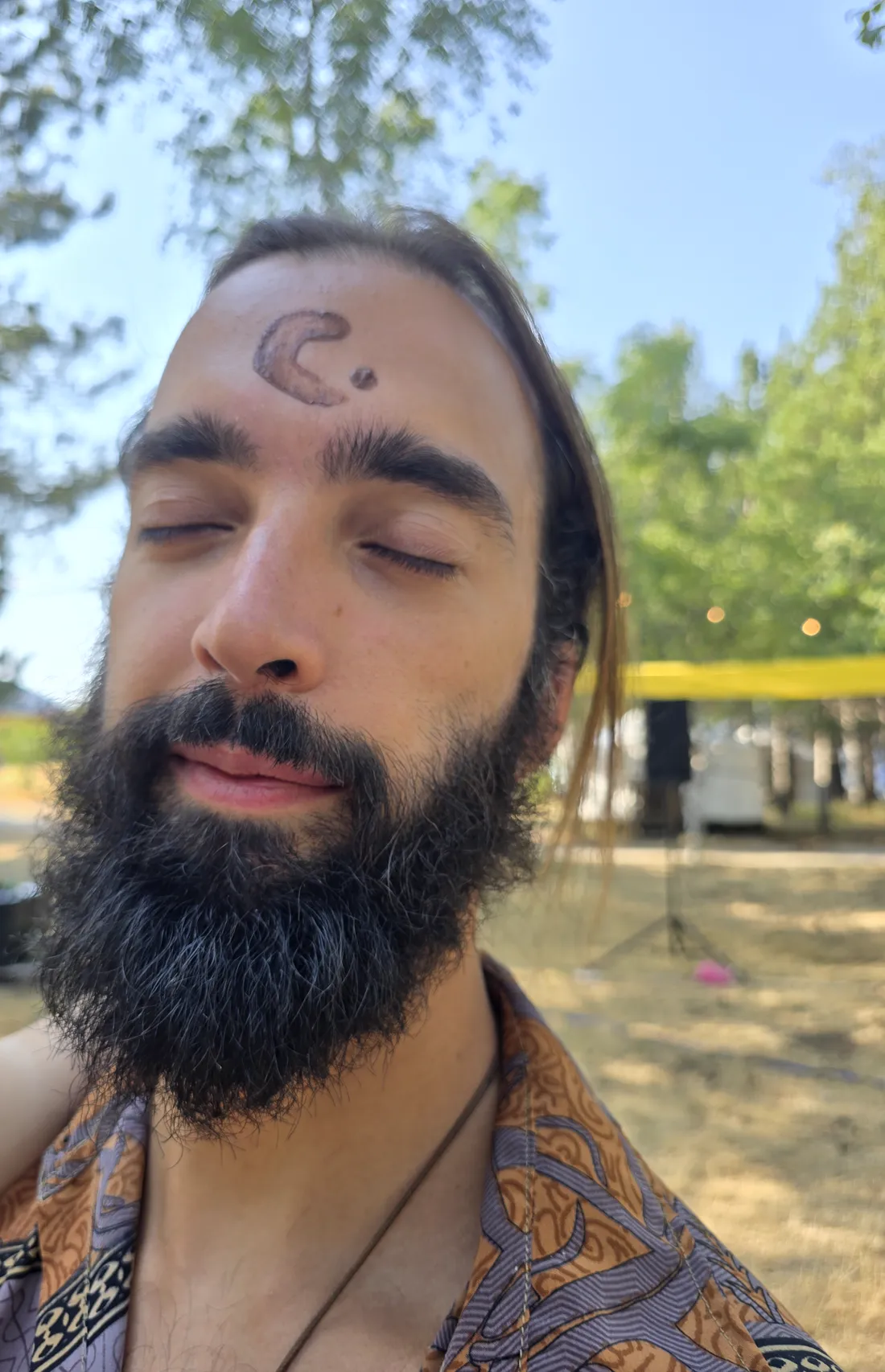 Tiago with his eyes closed and a moon drawn on his forehead, at a summer cacao gathering under the trees